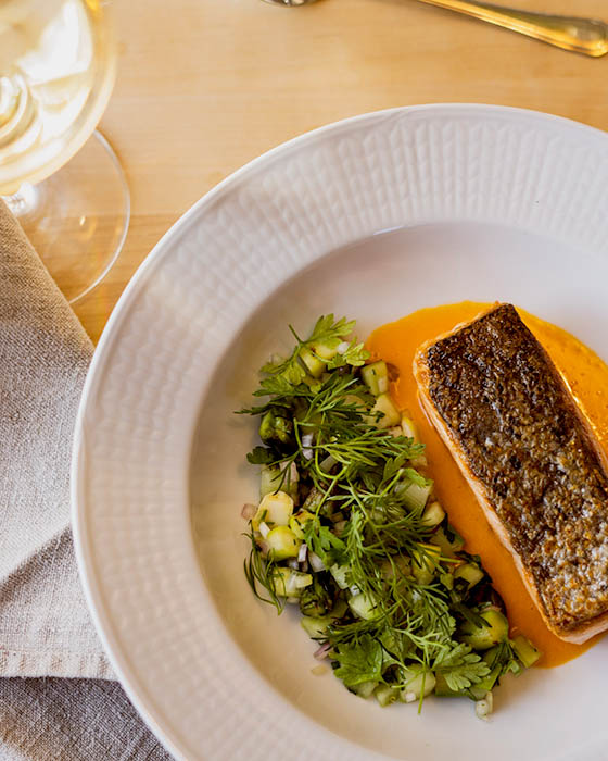 A beautiful dish of local salmon with a vegetable medley and a vibrant orange sauce on a white plate.